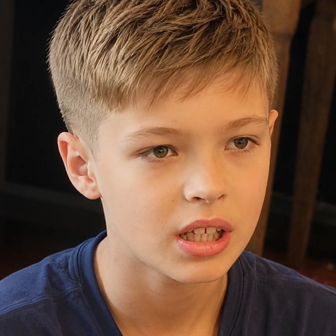 Young boy with short hair, wearing a blue shirt, looking intently while speaking.